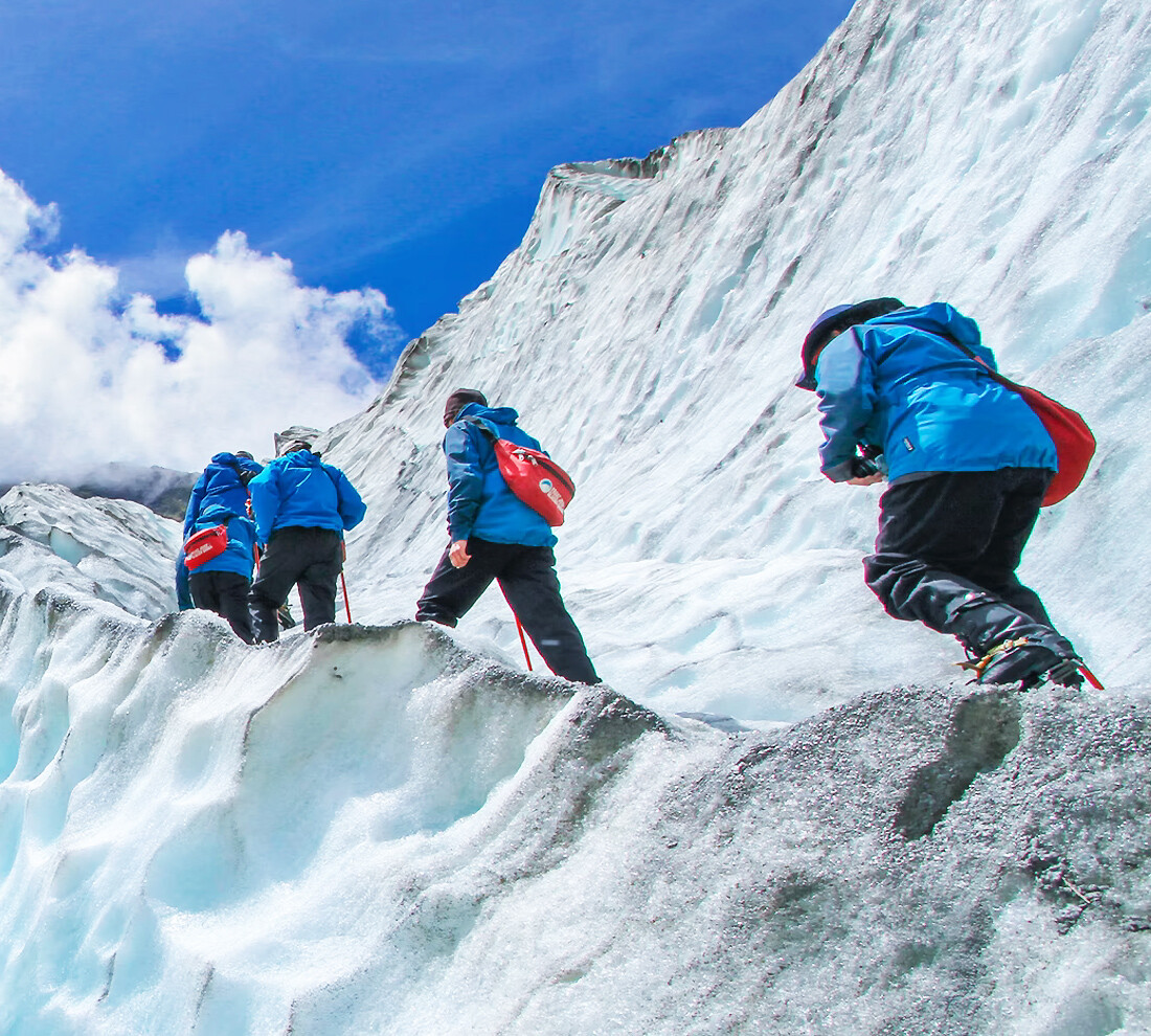 Ice Climbing Four men wearing blue jackets climbing up a mountain that is covered in ice and snow.