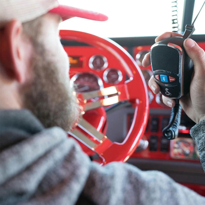 Cobra Lifestyle CB Man with beard driving a semi truck holding a Cobra CB radio microphone in his hand.