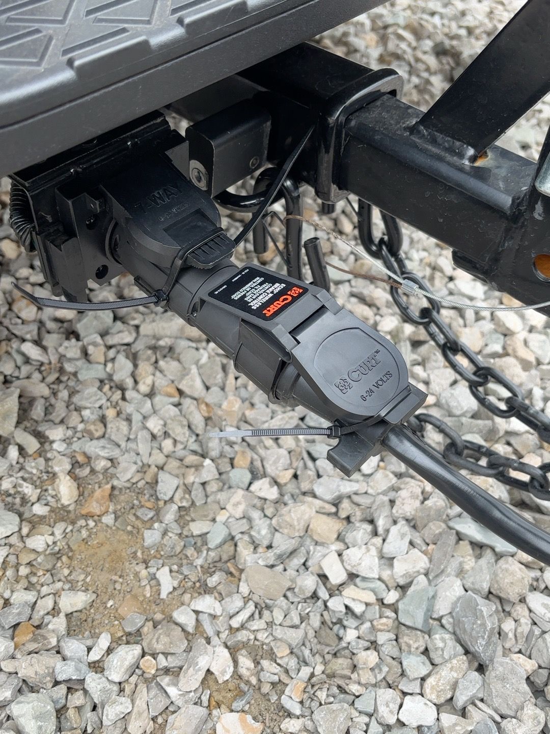 Curt Echo trailer brake controller connected at the seven-way plug near the travel trailer hitch and safety chains
