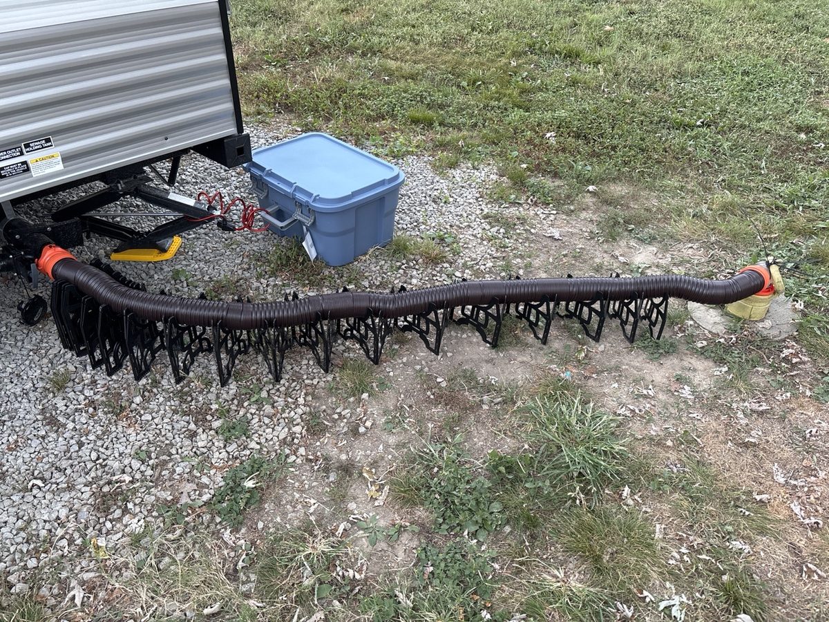 Black RV sewer hose and fittings laid out beside our KZ travel trailer