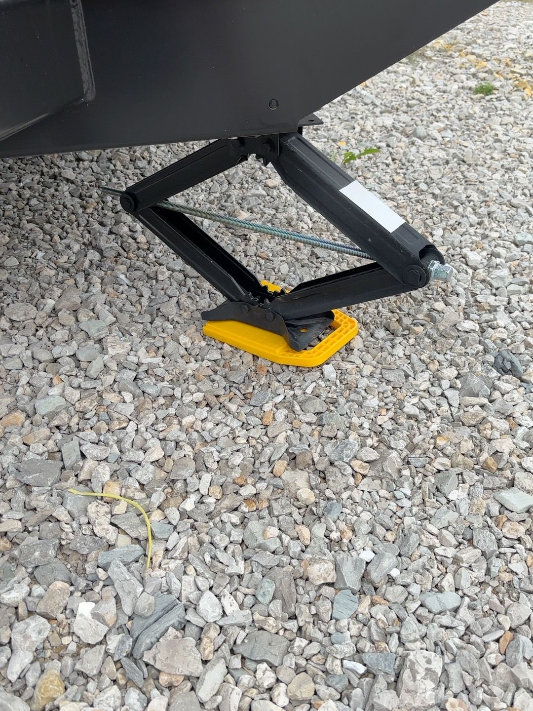 Travel trailer stabilizer jack lowered onto a yellow pad on gravel