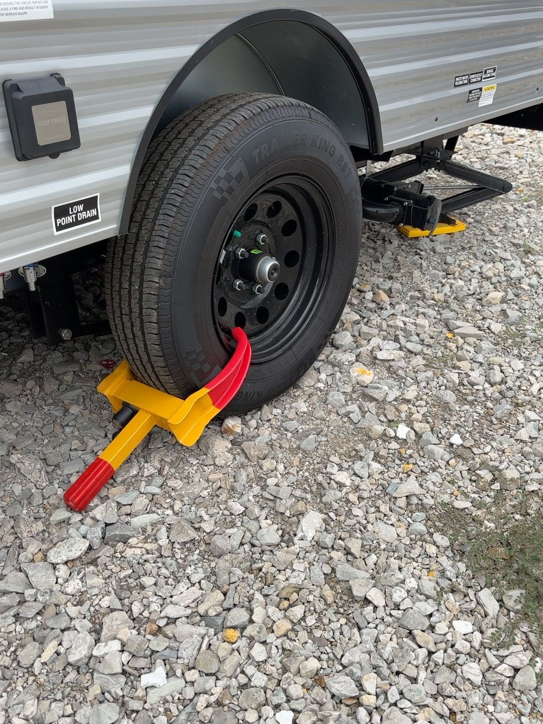 Red and yellow wheel chock secured against a KZ travel trailer tire on gravel